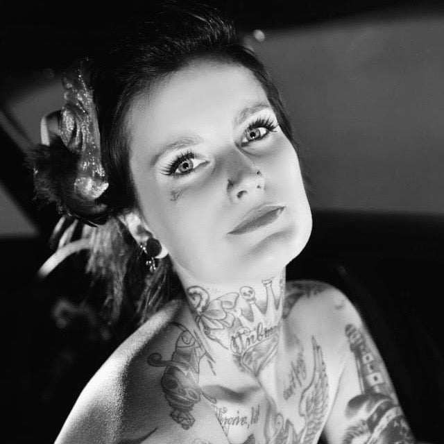 Black and white portrait of a woman with tattoos on her neck and arms.