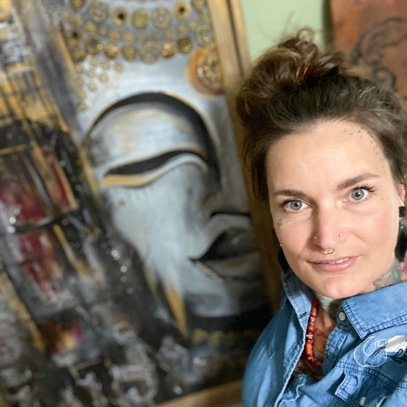 Woman standing in front of a painting of a mask with intricate details